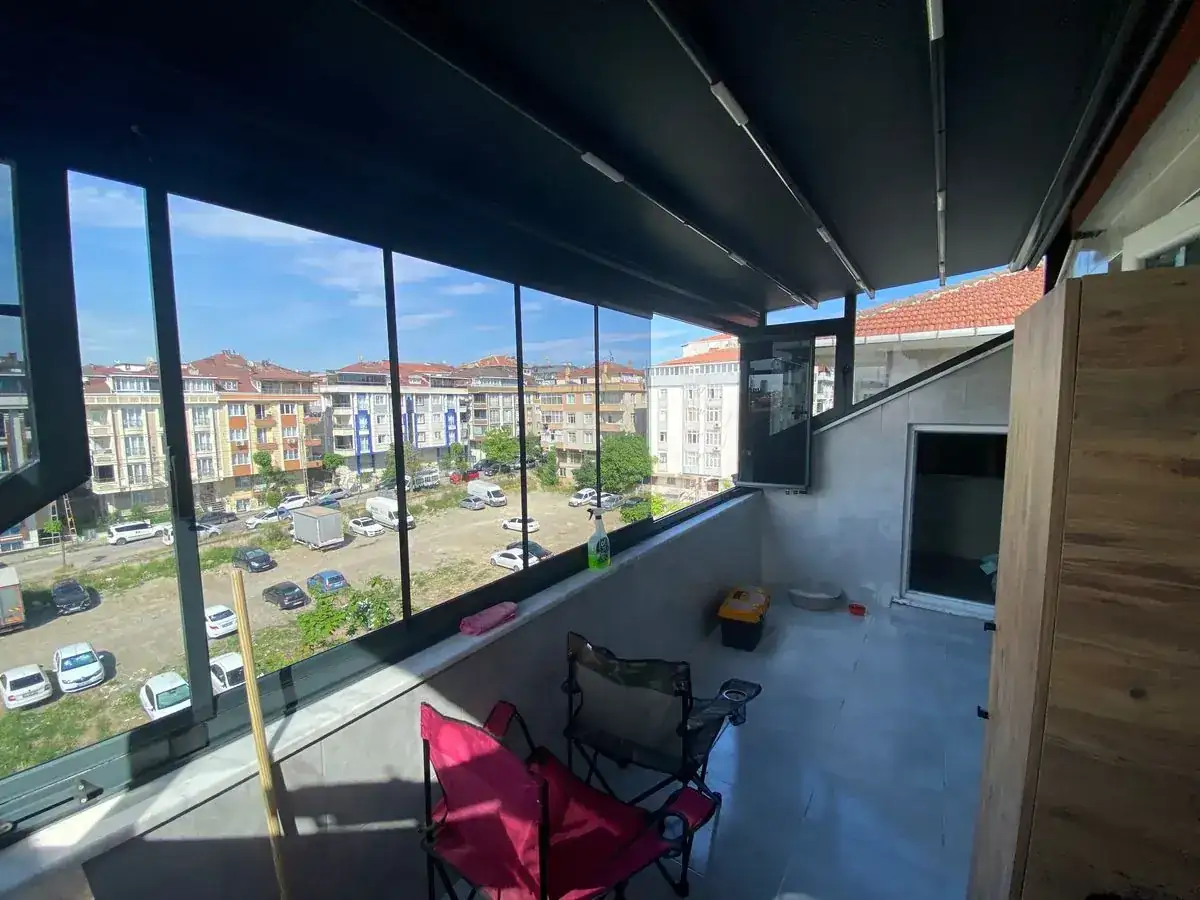 Çatı katı balkonunda motorlu pergola tavanı ve antrasit profilli cam balkon; bir kanat açılır pencere olarak açık