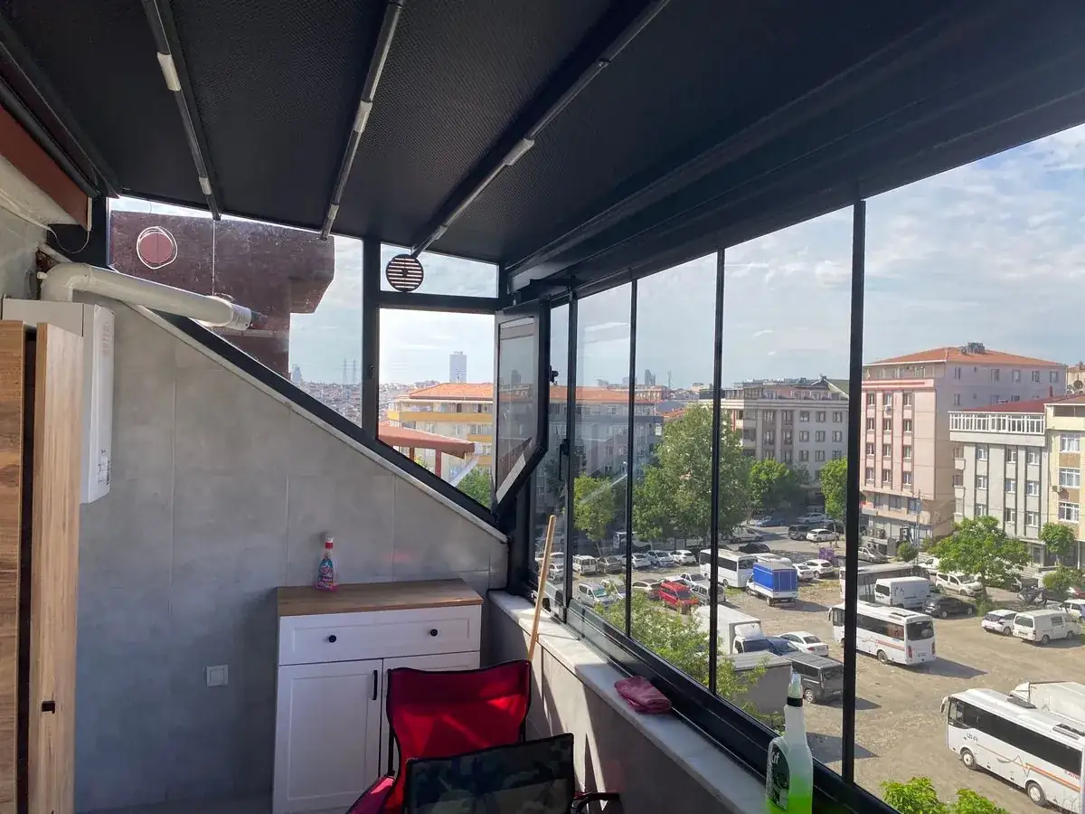 Aynı balkonun diğer yönü: eğimli duvara göre kesilmiş cam, üst camda yuvarlak havalandırma menfezi ve pergola rayları