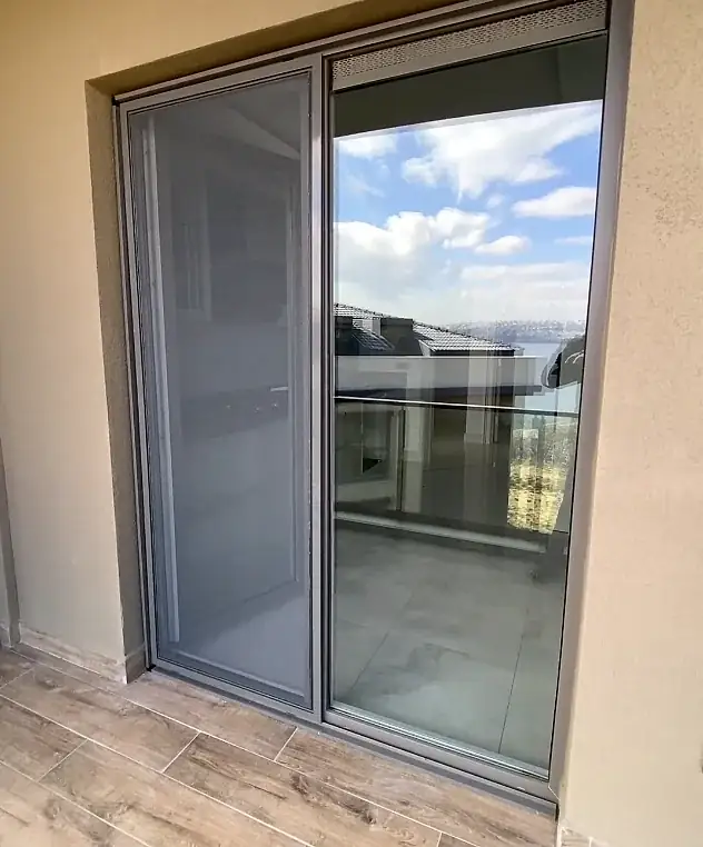 Balkon kapısına uygulanmış alüminyum kasalı sürgülü sineklik: solda tül kanadı, sağda sürme cam kapı